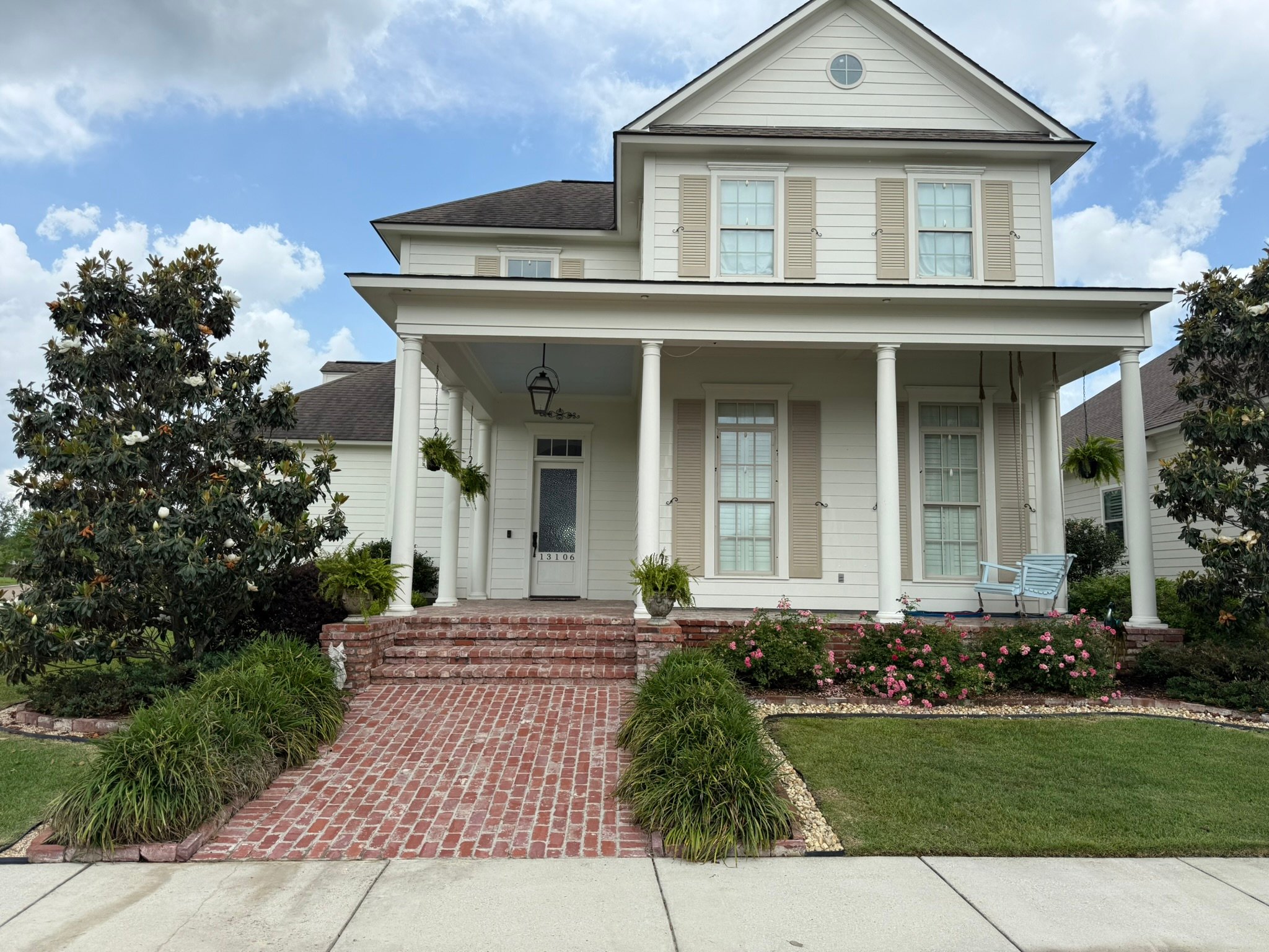 Clean white colonial home with brick porch, columns, and manicured landscaping