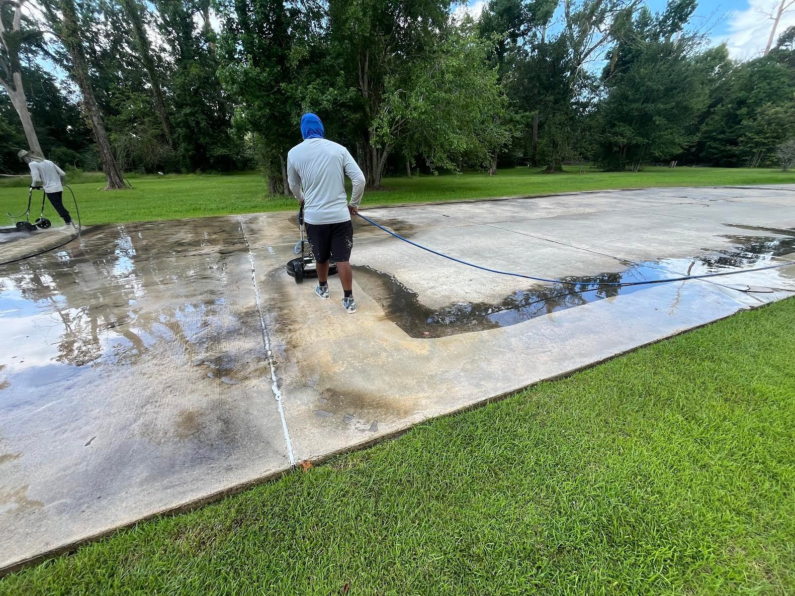 Technician pressure washing concrete driveway with blue hose, removing dirt and stains from patio surface