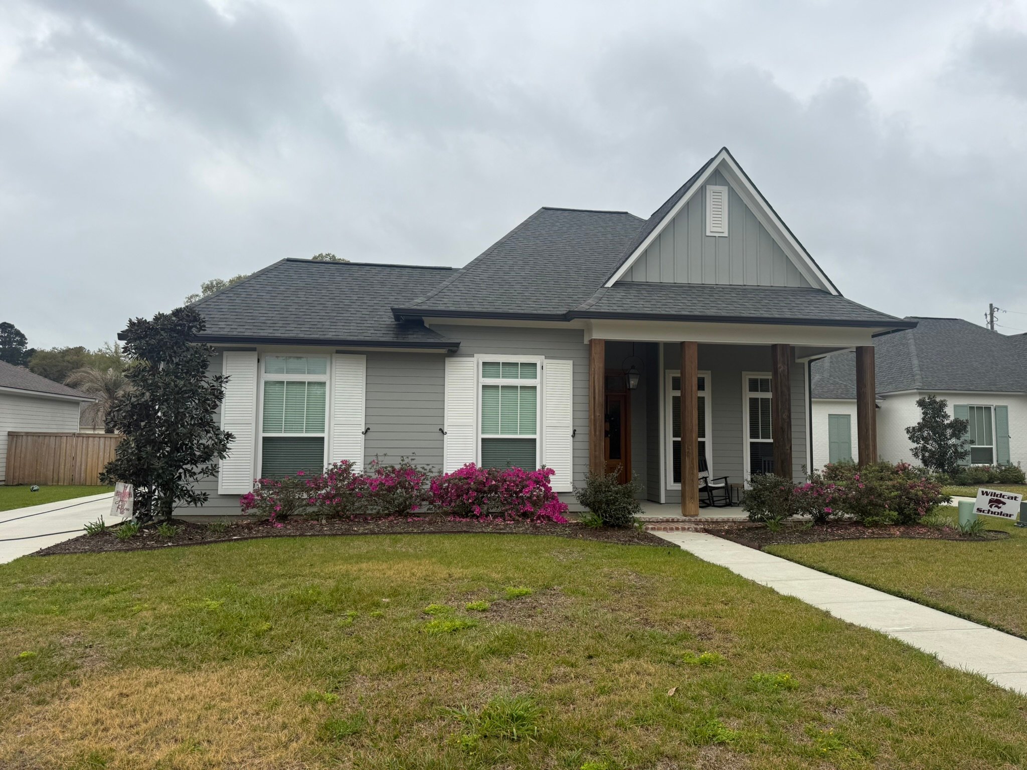 Clean white modern home with gray roof, wood porch columns, and magenta azaleas in front landscaping