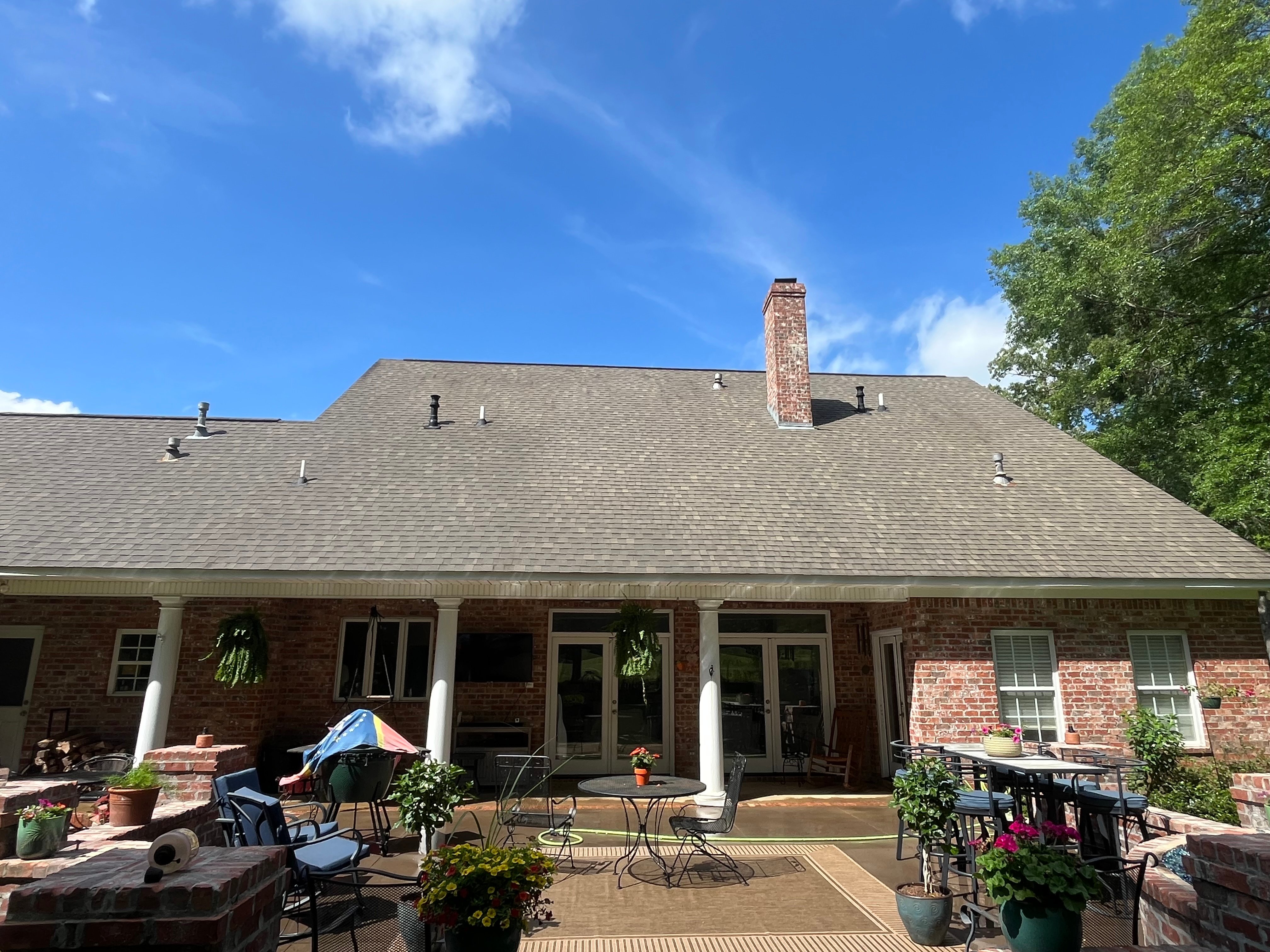 Clean gray asphalt shingle roof on brick home with white columns and patio area